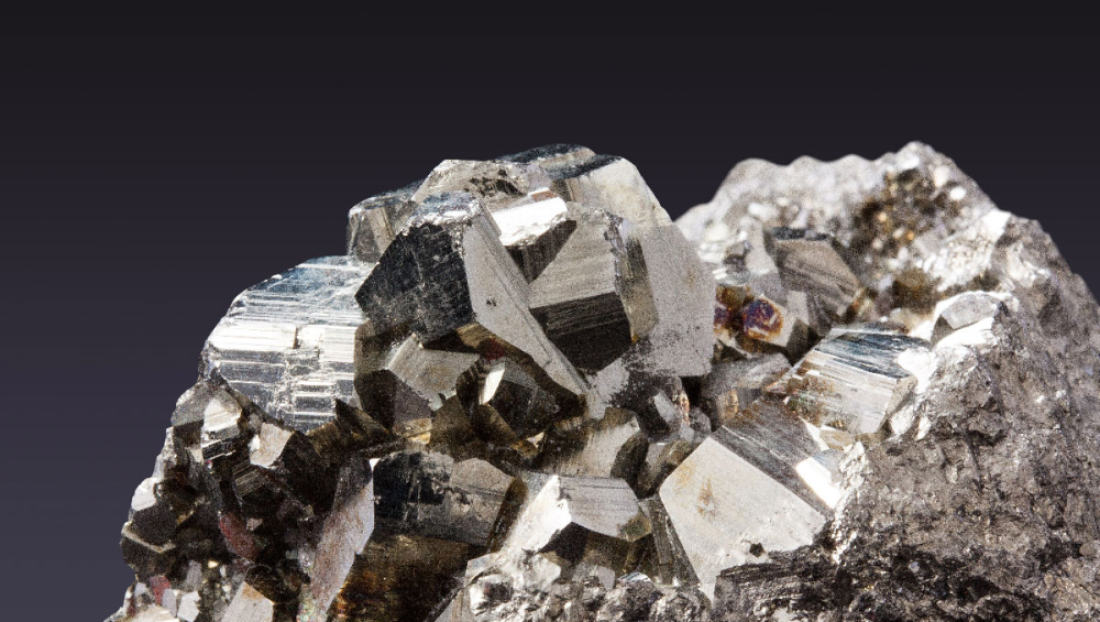 Extreme close-up of a metallic, silver-gold mineral cluster with sharp, geometric crystal formations.