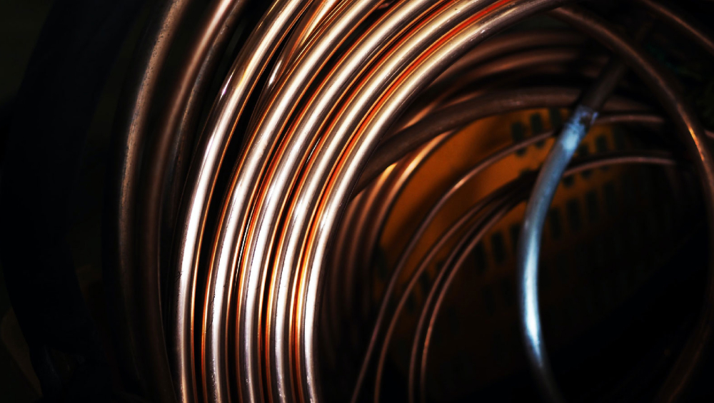 Coiled, shiny copper tubing or pipework, close-up with dramatic light reflections.