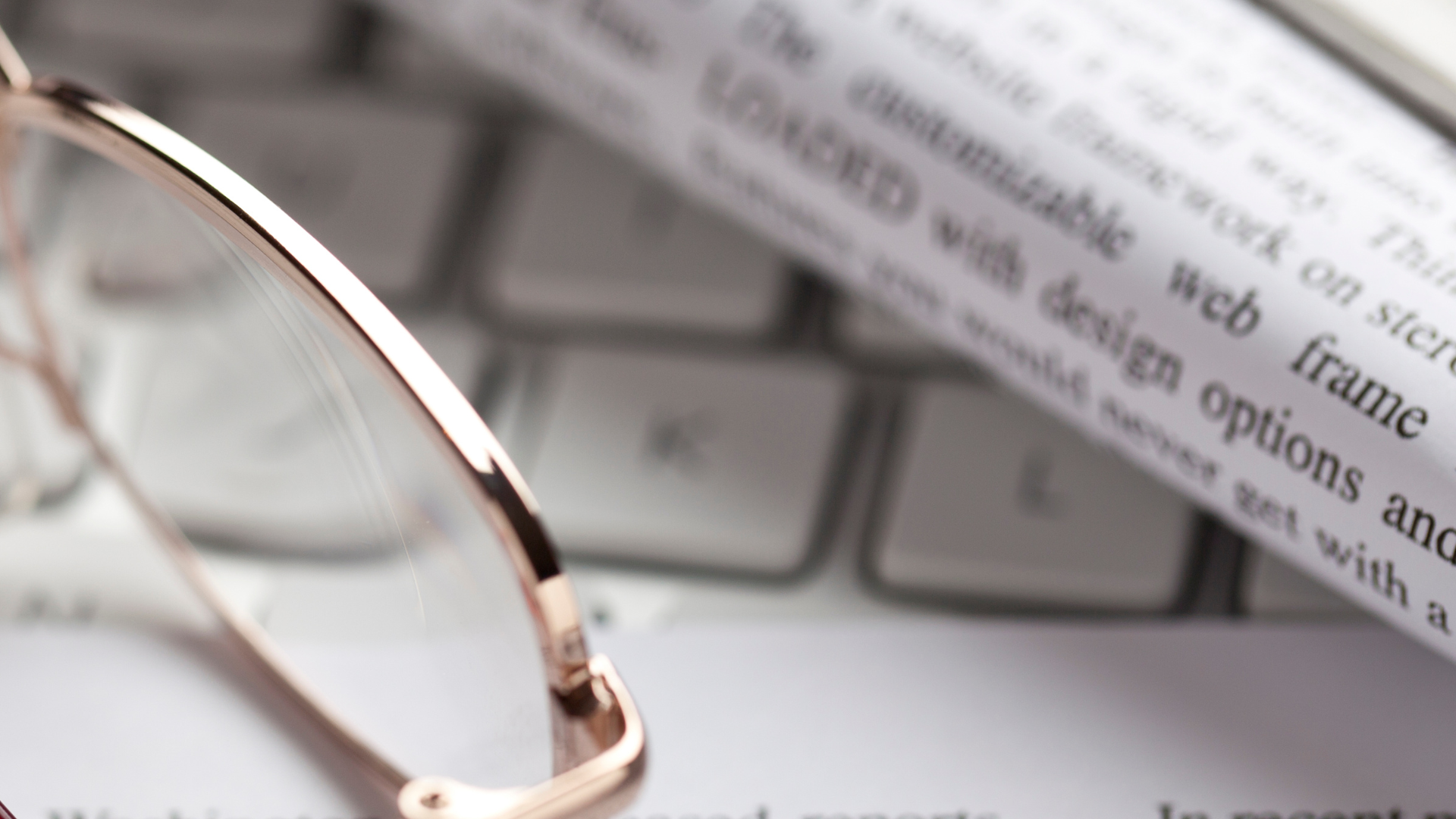 Close-up of reading glasses and a rolled newspaper/document resting on a computer keyboard.