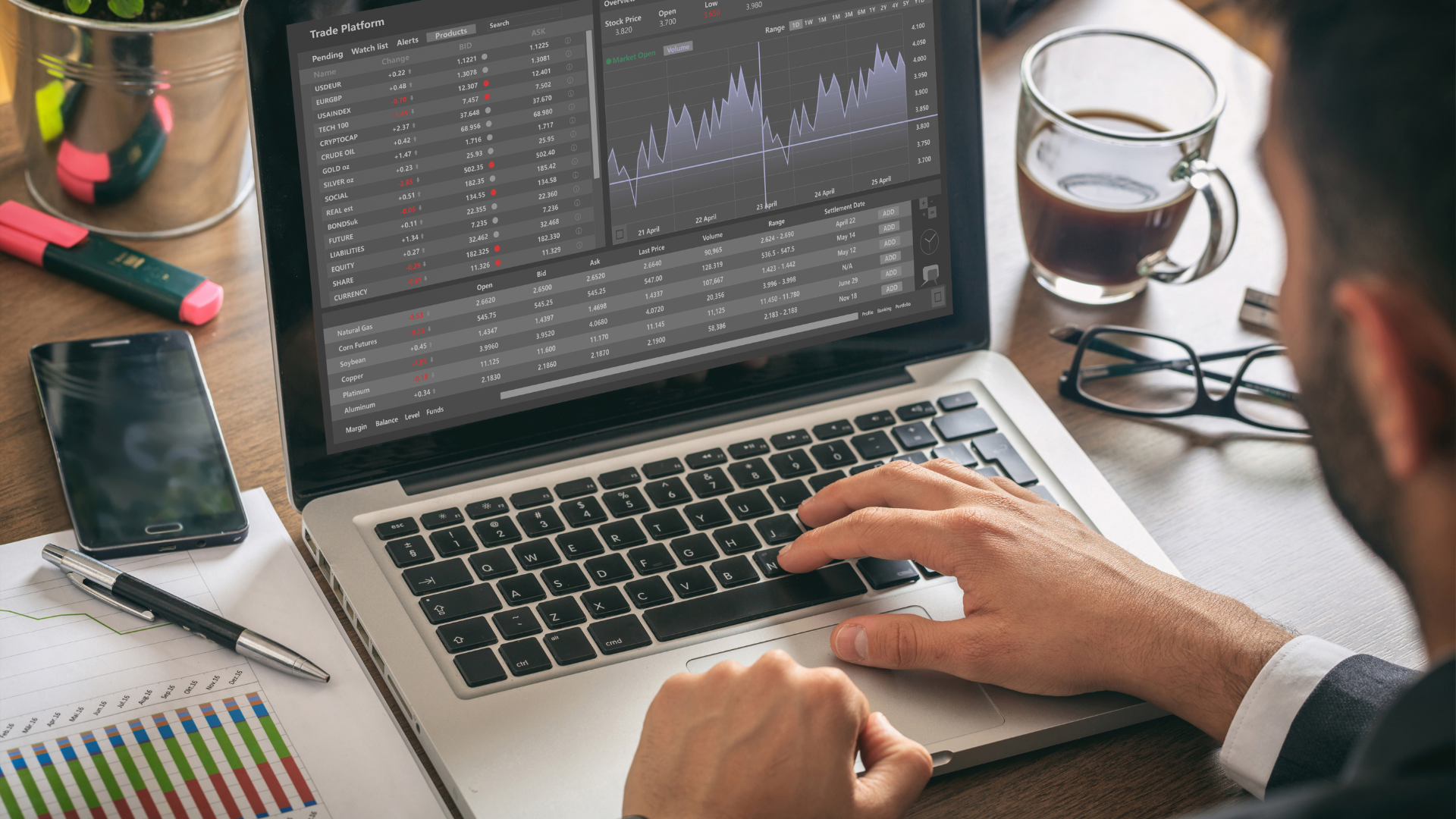 Over-the-shoulder view of a person typing on a laptop displaying a trade platform with stock charts, data, and market alerts.