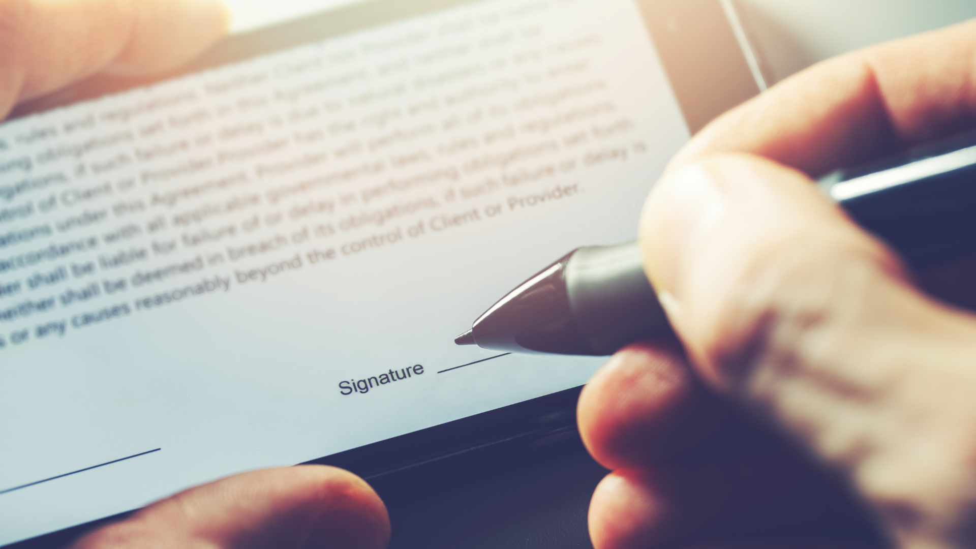 Extreme close-up of a hand using a stylus pen to digitally sign a contract on a tablet or smartphone screen.