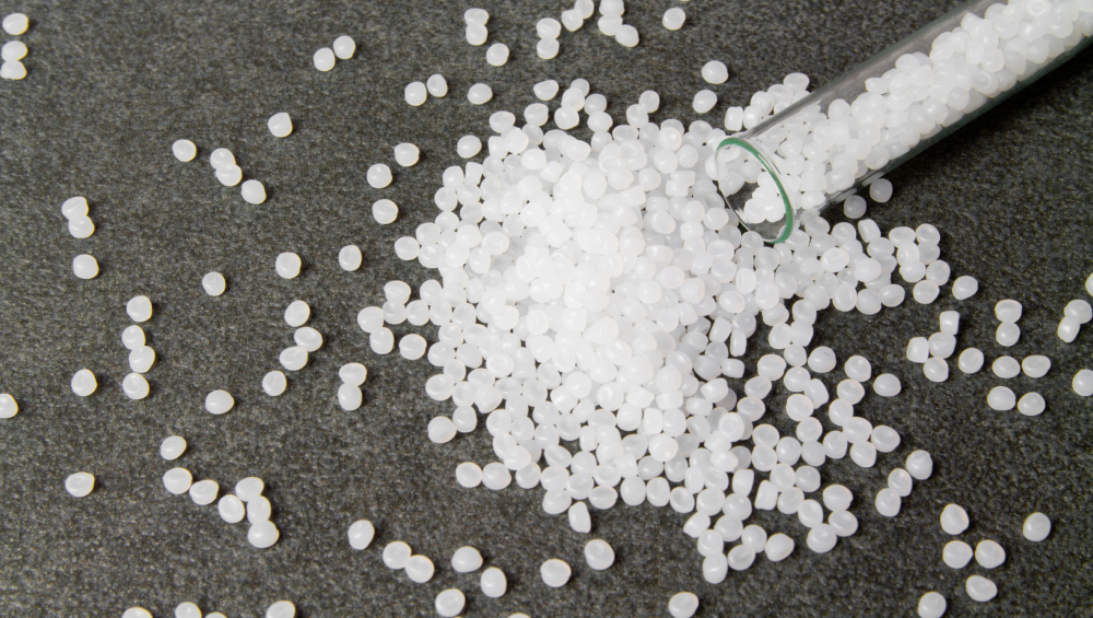 White plastic polymer pellets (resin) spilled out of a test tube onto a dark gray surface.
