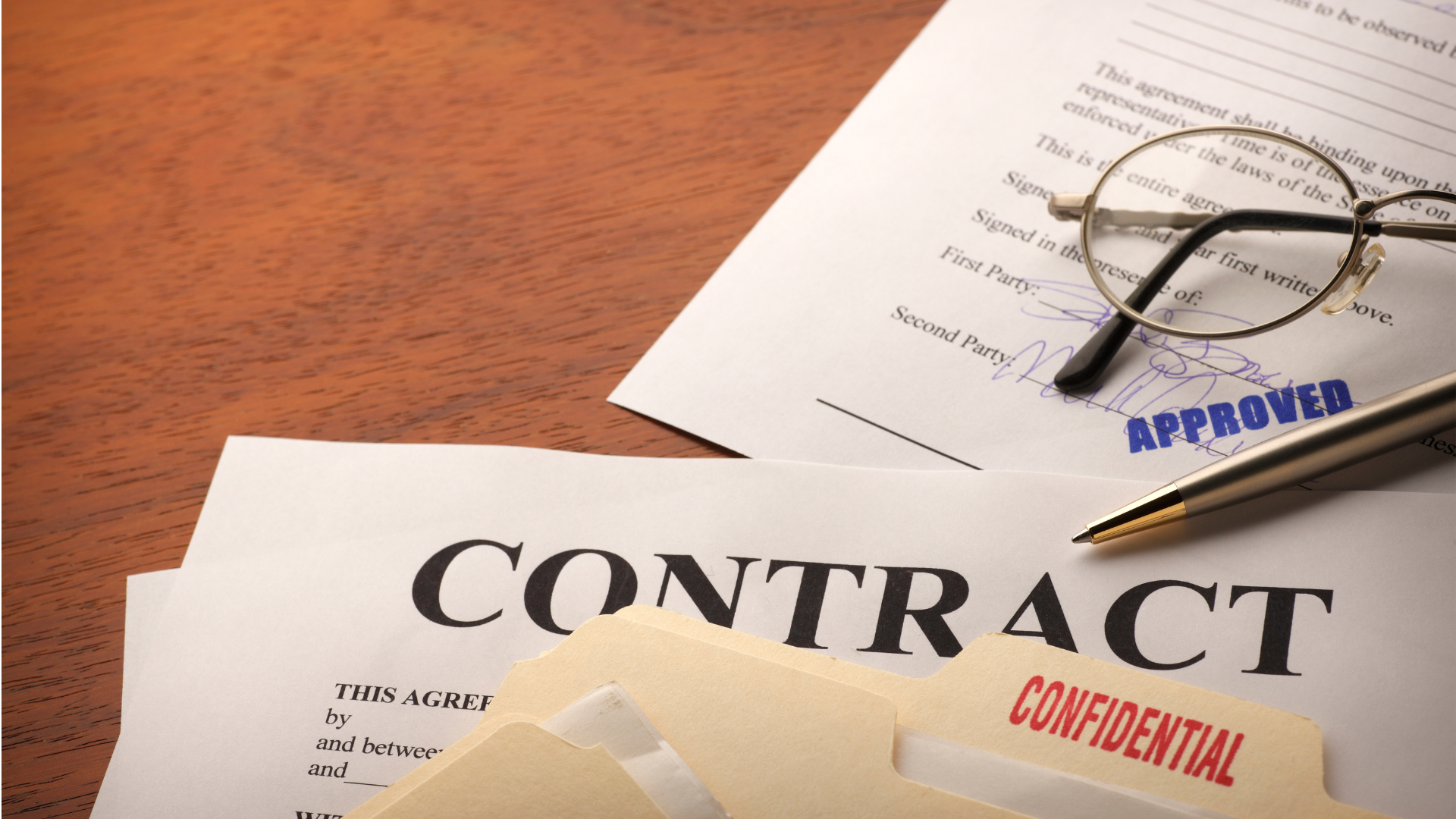 Close-up of a contract document marked "CONTRACT" and "APPROVED," with a pen and glasses resting near a signature line.