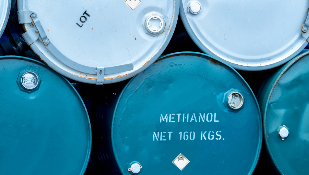 Stacked blue industrial barrels, one clearly labeled "METHANOL NET 160 KGS" with safety warning labels.