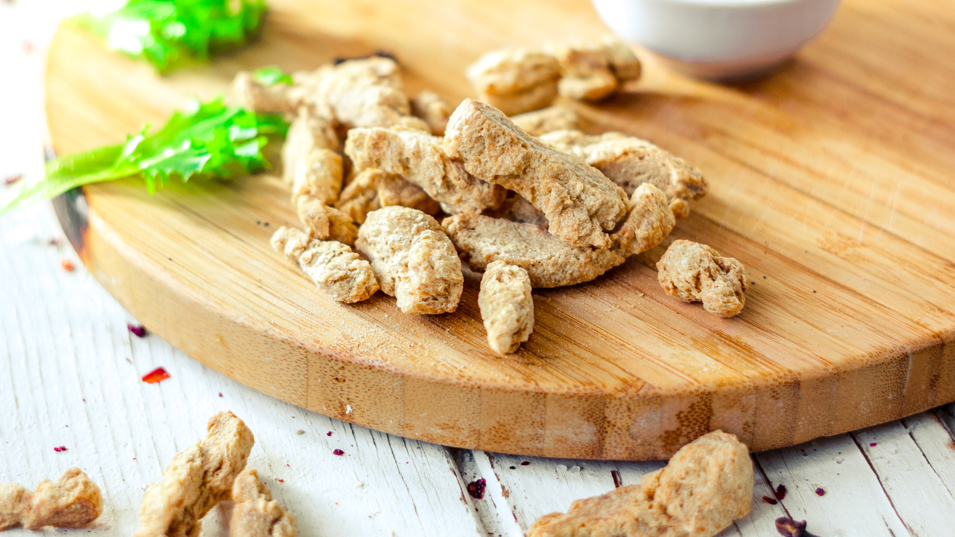 Textured Vegetable Protein (TVP) pieces piled on a round wooden cutting board with green leaves in the background.