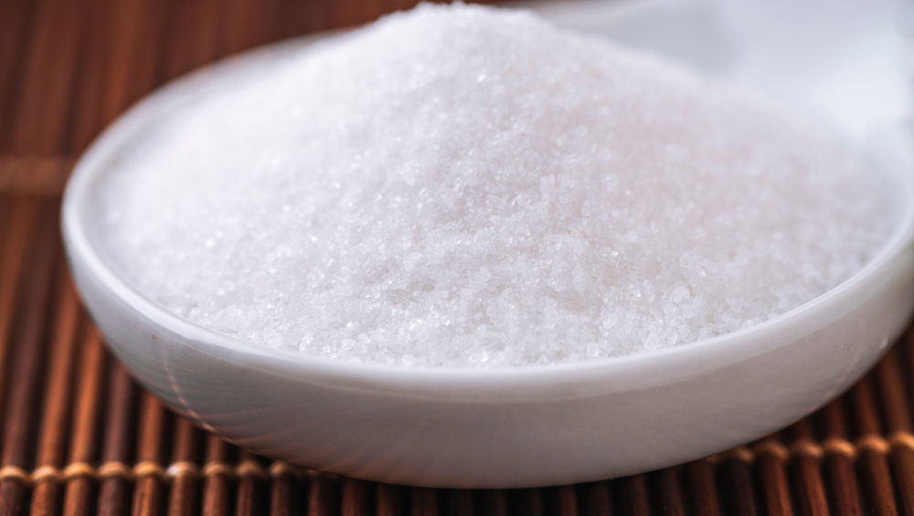 Close-up macro shot of a white ceramic bowl filled with a mound of fine white granulated sugar crystals.