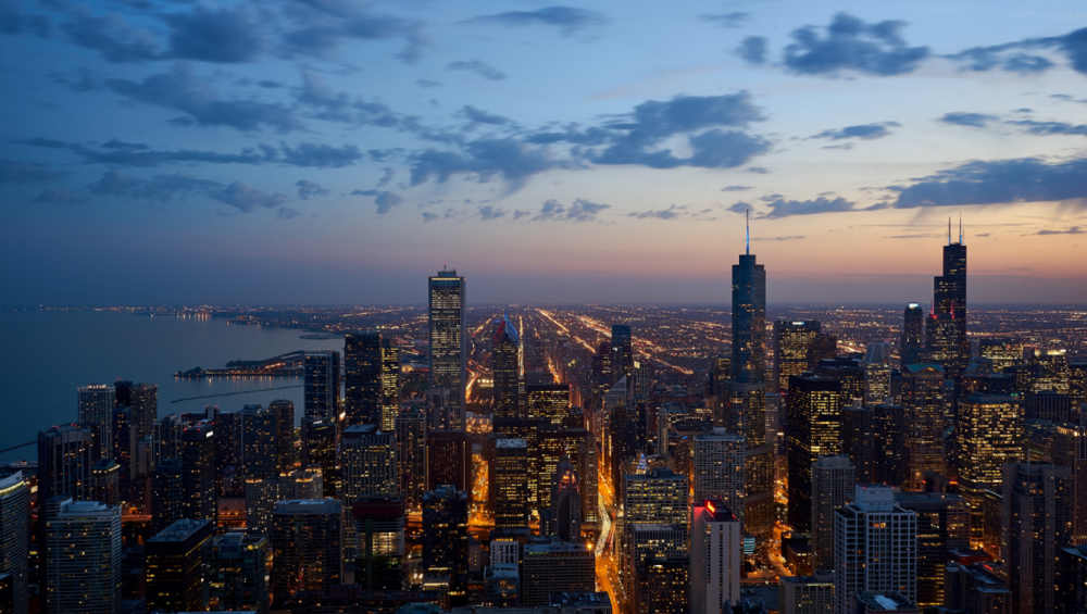High-angle panoramic view of the Chicago, Illinois, skyline at twilight, overlooking Lake Michigan and the illuminated cityscape.