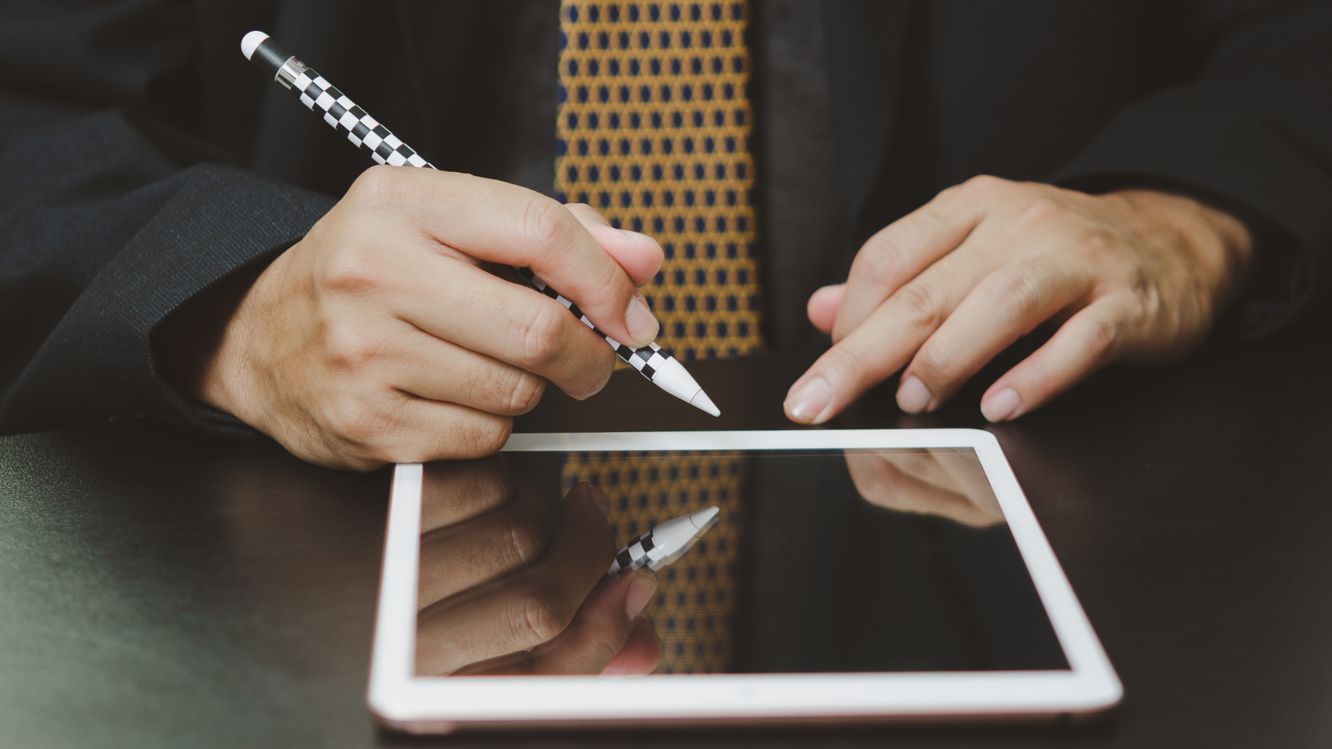 Businessperson using a stylus on a tablet at a desk.