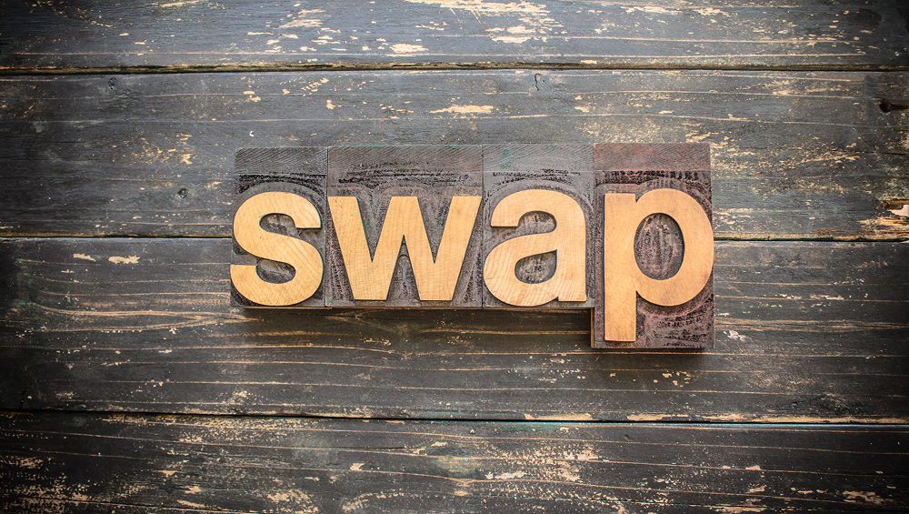The word "SWAP" spelled out in large gold wooden letterpress blocks on a dark, rustic wooden background.