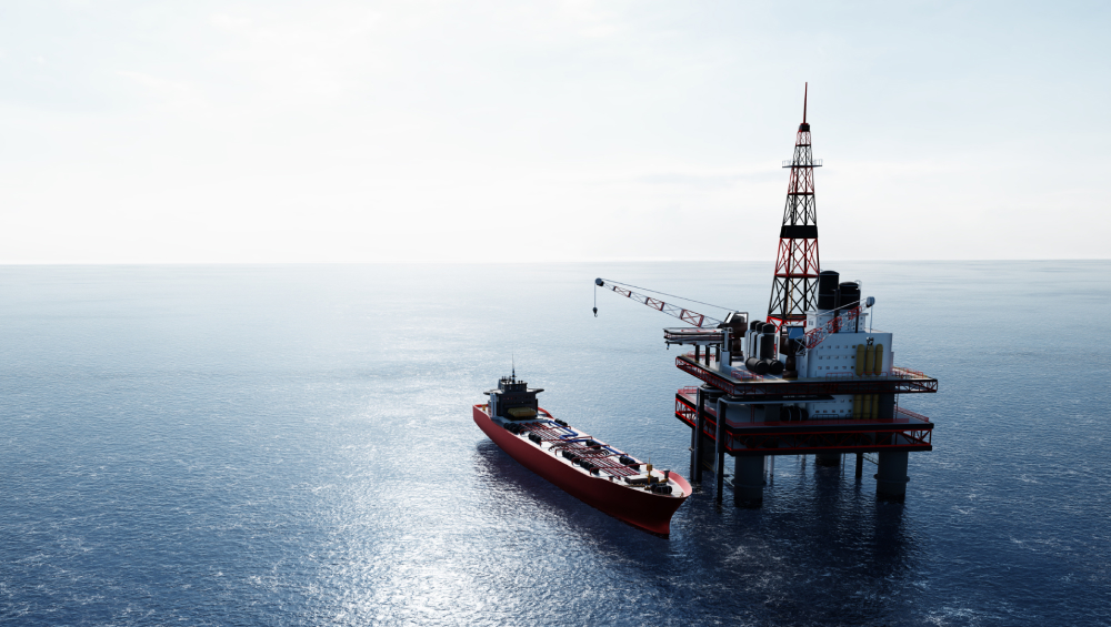 A red and white offshore oil drilling rig next to a red oil tanker ship floating on a calm blue ocean.