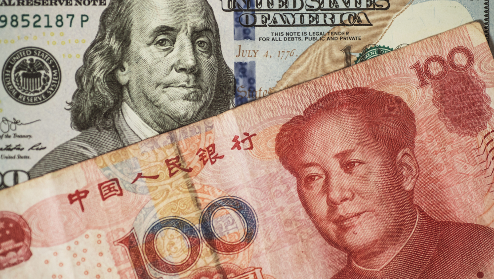 Close-up diagonal view of a US 100-dollar bill overlaid by a Chinese 100-Yuan Renminbi banknote, showing Franklin and Mao.