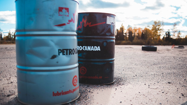 Two dented industrial metal barrels, labeled Petro-Canada, sitting on a dirt and gravel surface under an overcast sky.