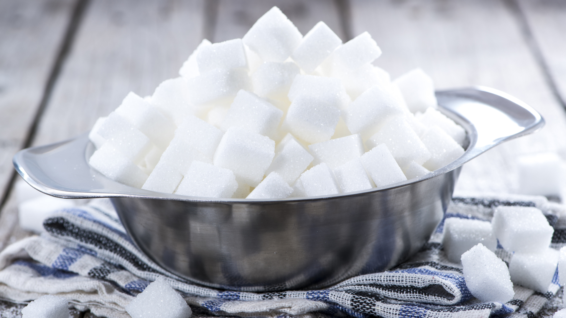 Stainless steel bowl overflowing with white sugar cubes on a kitchen cloth.