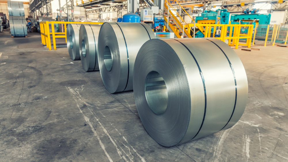Large rolls of galvanized steel sheet metal lined up on an industrial factory floor.