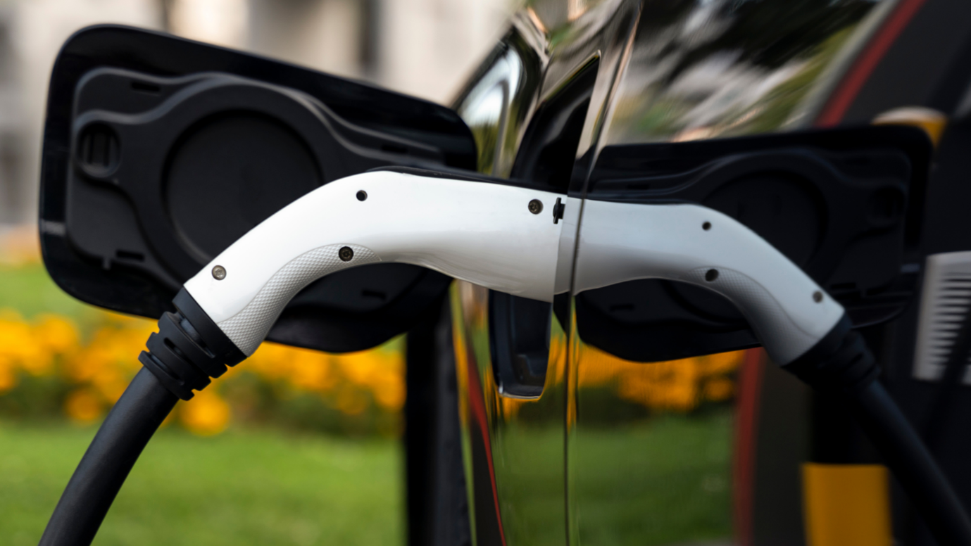 Close-up of a white electric vehicle charging nozzle plugged into a black car.