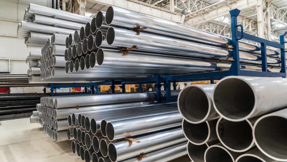 Stacks of bright, silvery round metal pipes or tubes stored on blue industrial racking in a warehouse.
