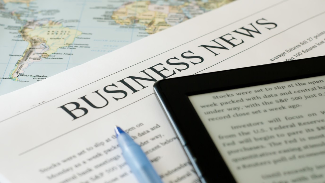 Newspaper titled “Business News” beside a tablet displaying financial text.