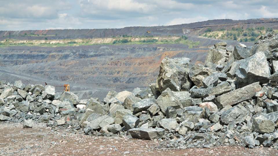 Large open pit mine landscape with a foreground pile of broken grey rocks and distant mining terraces.