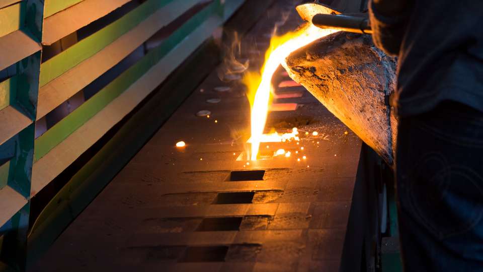 Foundry worker pouring molten metal from ladle into molds.