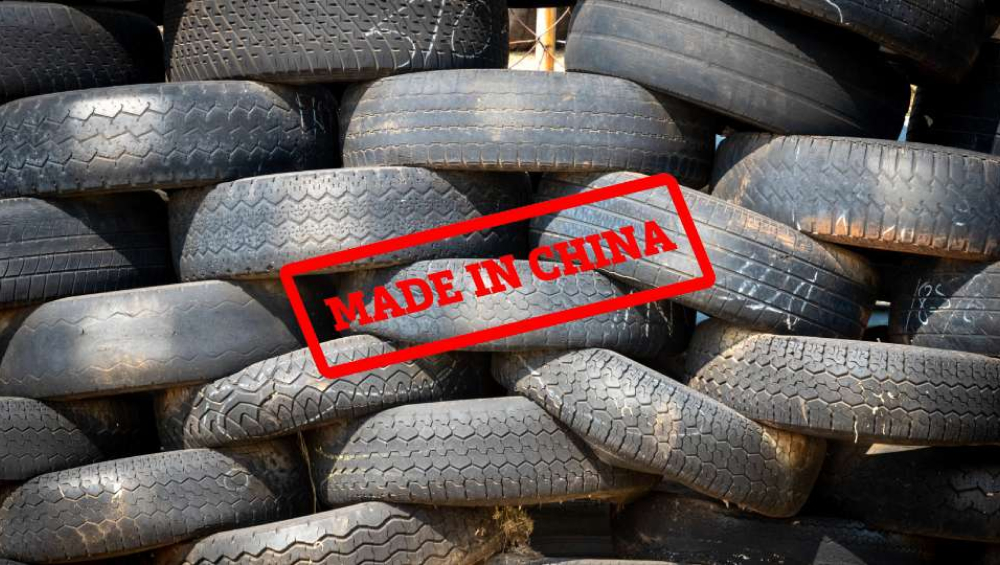 A large, chaotic pile of used or recycled vehicle tires overlaid with a red stamp graphic reading "MADE IN CHINA."