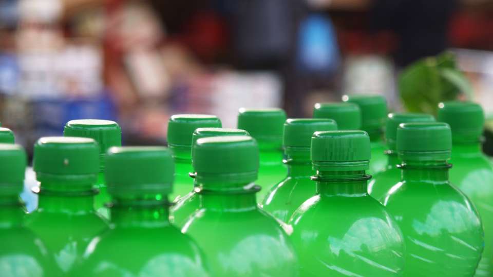 Close-up of the tops of rows of identical clear or light green plastic bottles with matching solid green caps.