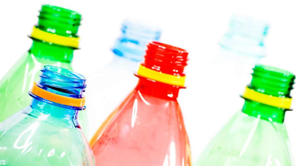 Close-up of the necks of several empty, brightly colored plastic bottles (green, blue, red) against a white background.