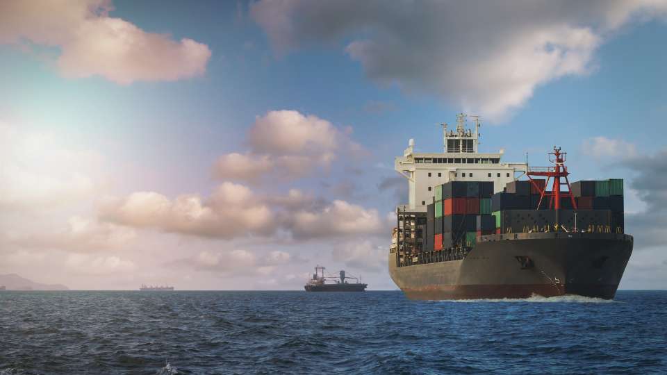 Large cargo container ship sailing on choppy ocean water under a cloudy, dramatic sky.
