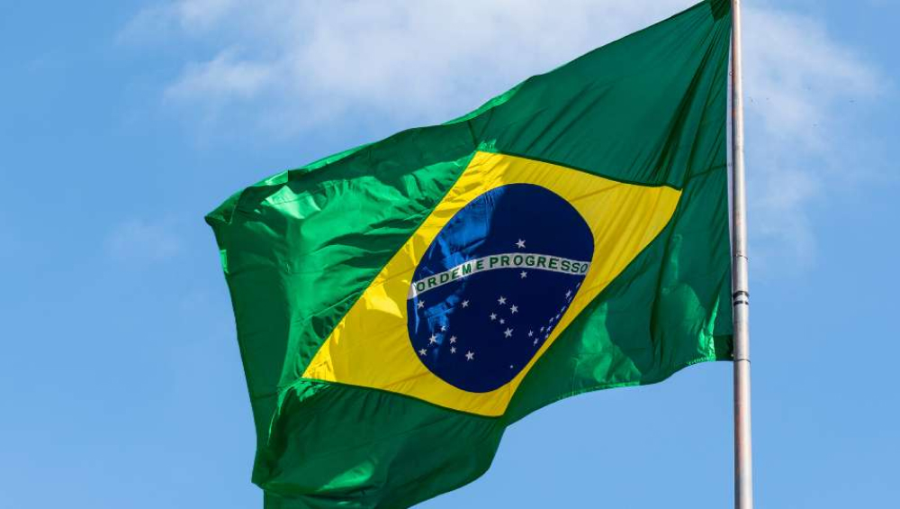 The national flag of Brazil waving against a blue sky with some clouds.