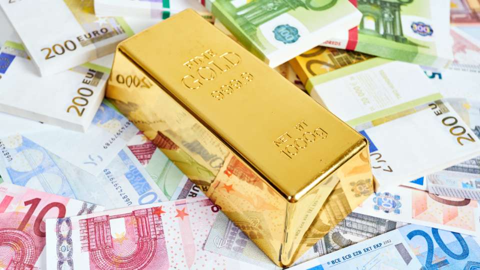 Single 1000g gold bar resting on a scattered background of Euro bank notes.