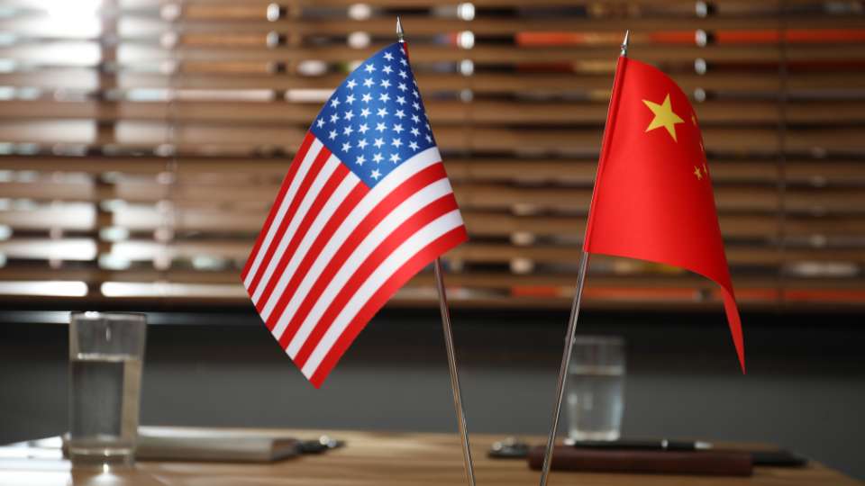 Miniature flags of the United States and China standing next to each other on a conference table.