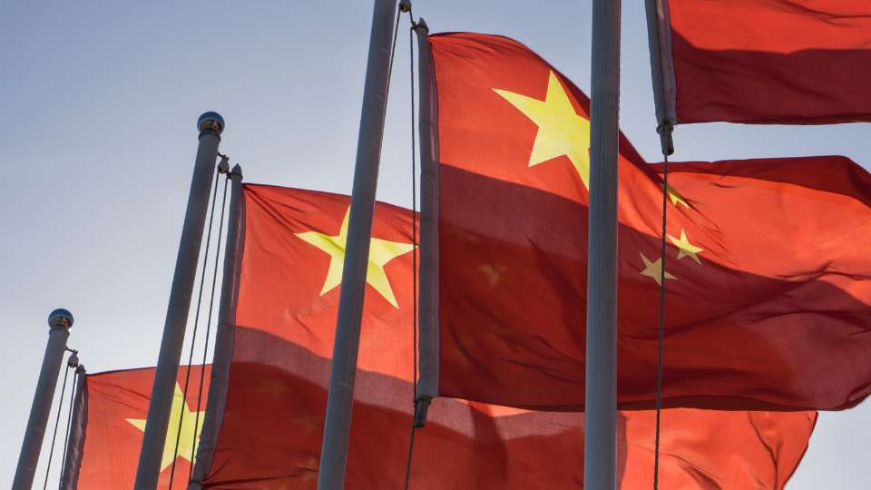 More than 1 Chinese flag waving in daylight, highlighting China’s influence on global markets.