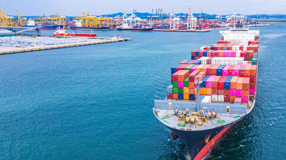 Container ship transporting cargo containers across a busy port waterway.