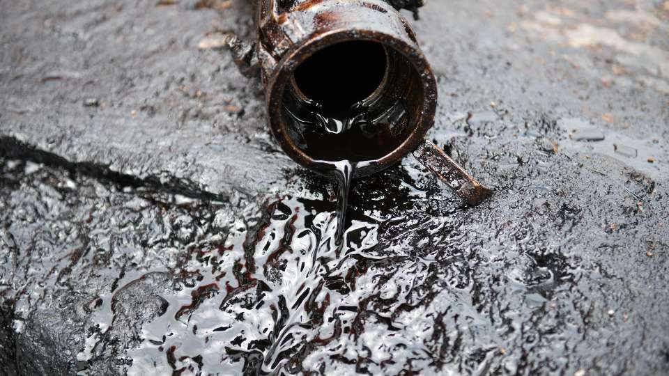 Crude oil leaking from a metal container onto the ground.