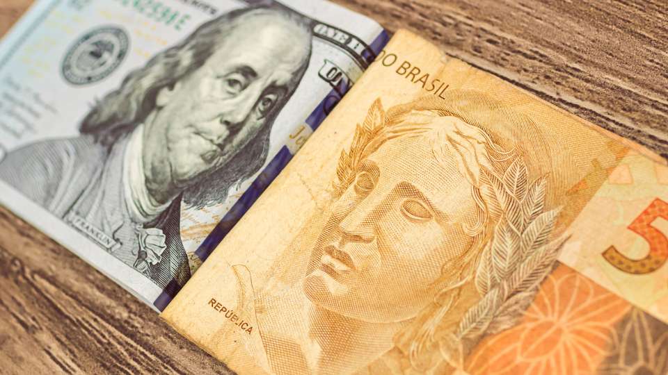 Close-up of a Brazilian 50 Real bank note overlapping US Dollar bills ($100 and $1), symbolizing the exchange rate.