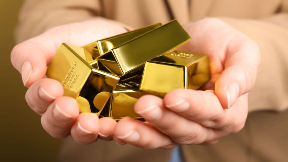 Cupped hands holding a pile of small, shiny gold bars or ingots, symbolizing security and saving.