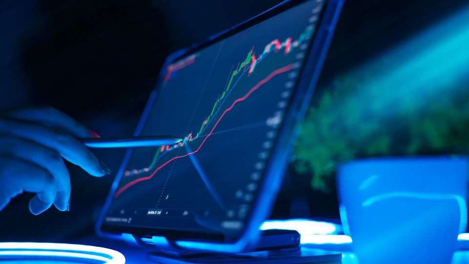 Tablet screen showing rising stock market chart with a hand holding a stylus.
