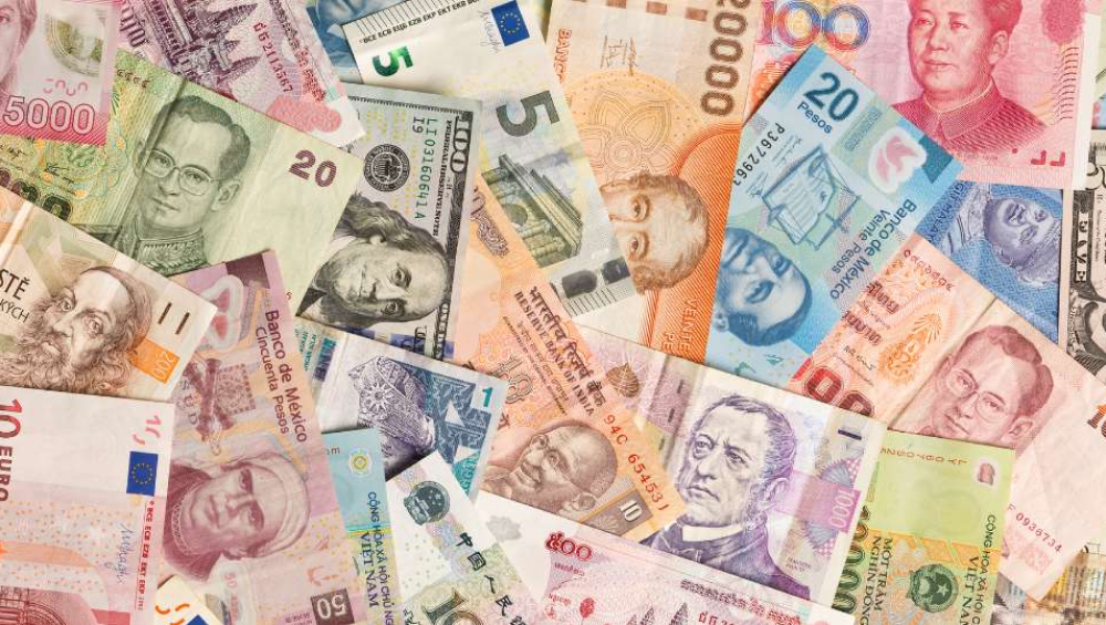 A close-up collage of scattered, overlapping international bank notes and world currencies, including USD, Euro, and Asian currencies.