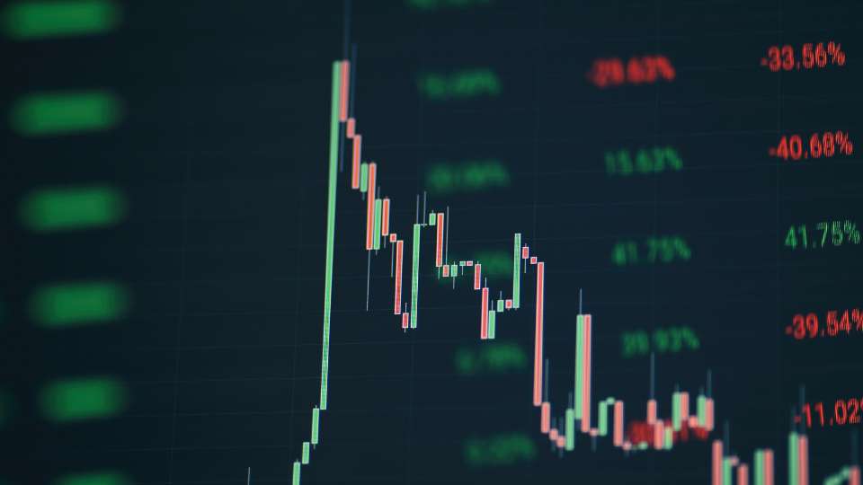 Close-up of a downward-trending financial candlestick chart on a dark screen, indicating a market decline.