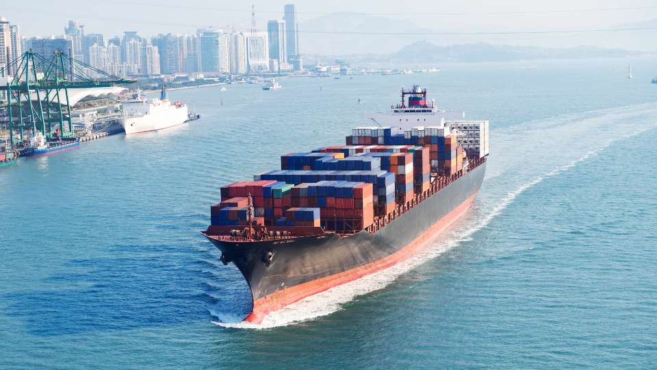 Container ship transporting cargo containers across a busy port waterway.