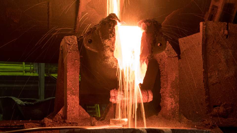 Foundry worker pouring brilliant orange molten metal into a casting channel.