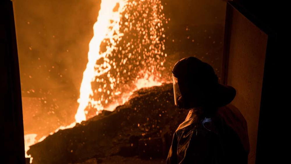 A worker in protective gear standing near molten metal pouring in a smelting facility.