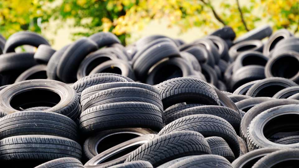 A massive pile of black, discarded vehicle tires stacked high in a scrap yard or recycling facility.