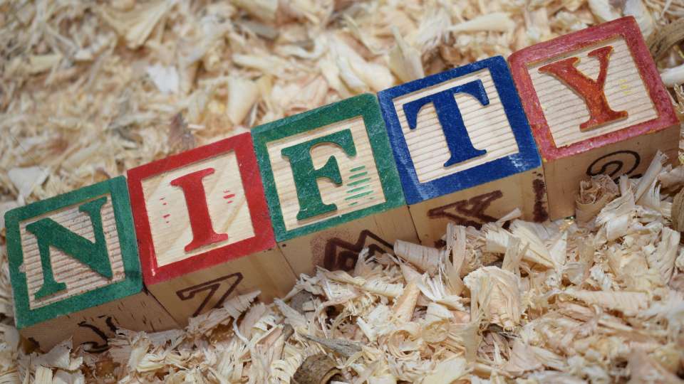 Wooden alphabet blocks spelling the word "NIFTY" on wood shavings.