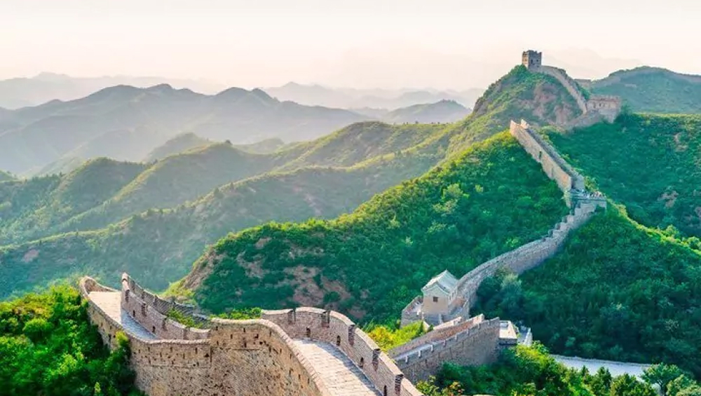 The Great Wall of China winding along the ridges of lush green mountains.
