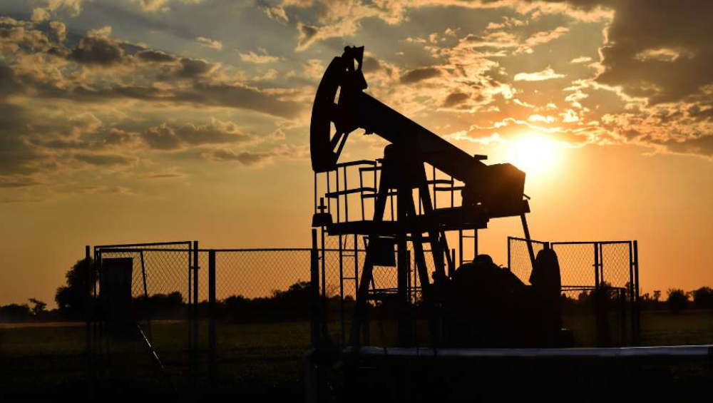 Silhouette of an industrial oil pump jack operating against a sunset sky.
