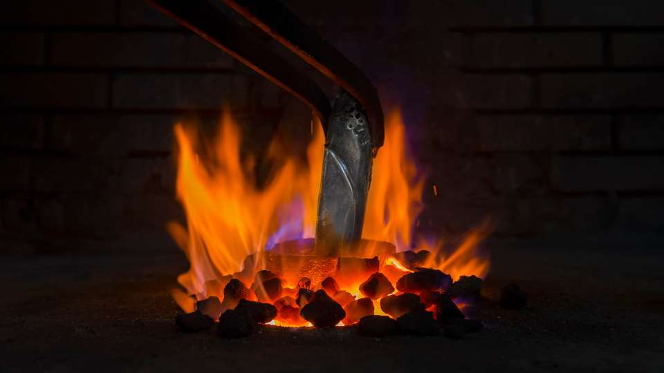Glowing red-hot metal being heated in a blacksmith's coal forge.