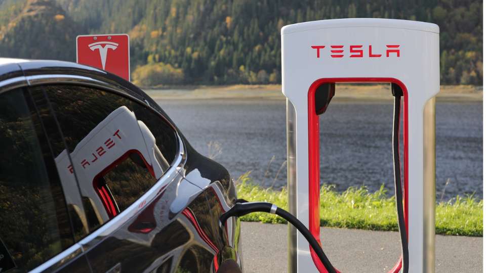 Black Tesla electric vehicle plugged into a Supercharger station near a lake.