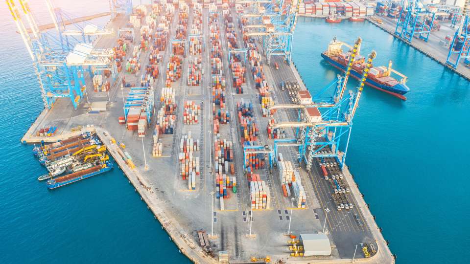 Aerial drone view of a busy cargo port with cranes and container ships.