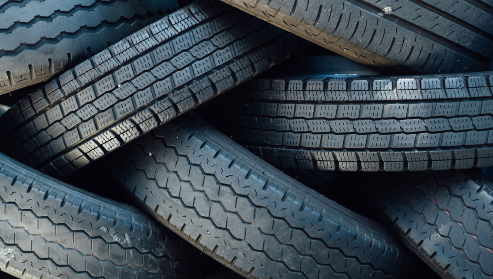 Close-up of a dense pile of dark, worn car tires with various tread patterns.