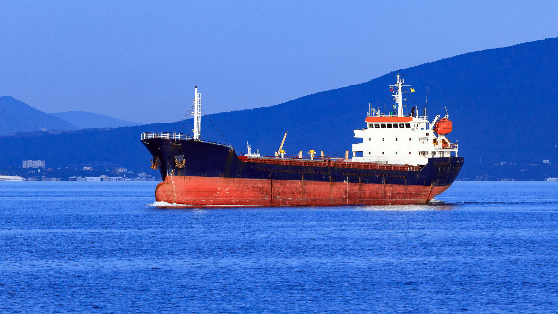 Large commercial cargo ship sailing on blue water with a mountain backdrop